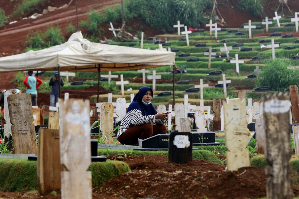 A woman performs a prayer next to a grave in the Pondok Rangon public cemetery designated for Covid-19 victims on Dec. 2, 2020. The cemetery in East Jakarta is now out of space due to surging number of coronavirus-related deaths in the capital city. (Beritasatu Photo/Joanito De Saojoao)