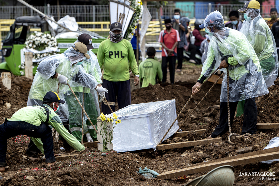 Funeral workers lower the coffin of a Covid-19 patient at Srengseng Sawah public cemetery in South Jakarta on Jan. 26, 2021. (JG Photo/Yudha Baskoro)