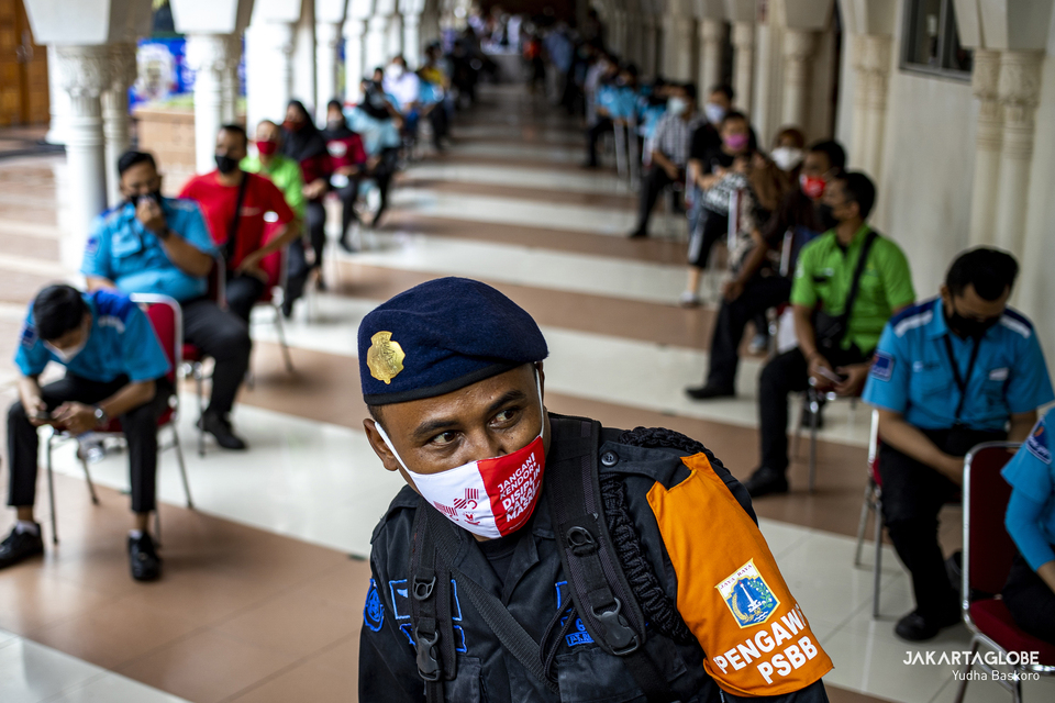 A policeman stands guard in front as traders wait in line for their turn for Covid-19 vaccination at Tanah Abang Market, Central Jakarta on Feb. 17, 2021. (JG Photo/Yudha Baskoro)