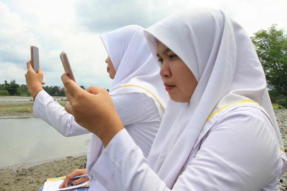Two nursing students take online learning by the river to find a signal in  Keutambang, Pante Ceuremen, West Aceh on August 26, 2020. (Antara Photo/Syifa Yulinnas)