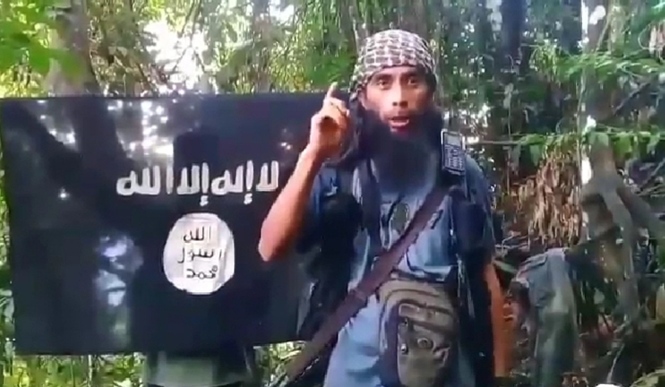 A screen capture from a video shows purported Ali Kalora speaks in front of an ISIS flag. (Videography)