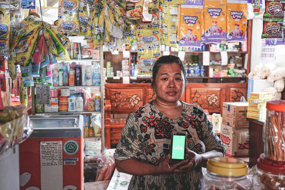 This undated photo showed a shop owner in Malang, East Java, stands in her shop and shows Ula app on her smartphone. (Photo courtesy of Ula)