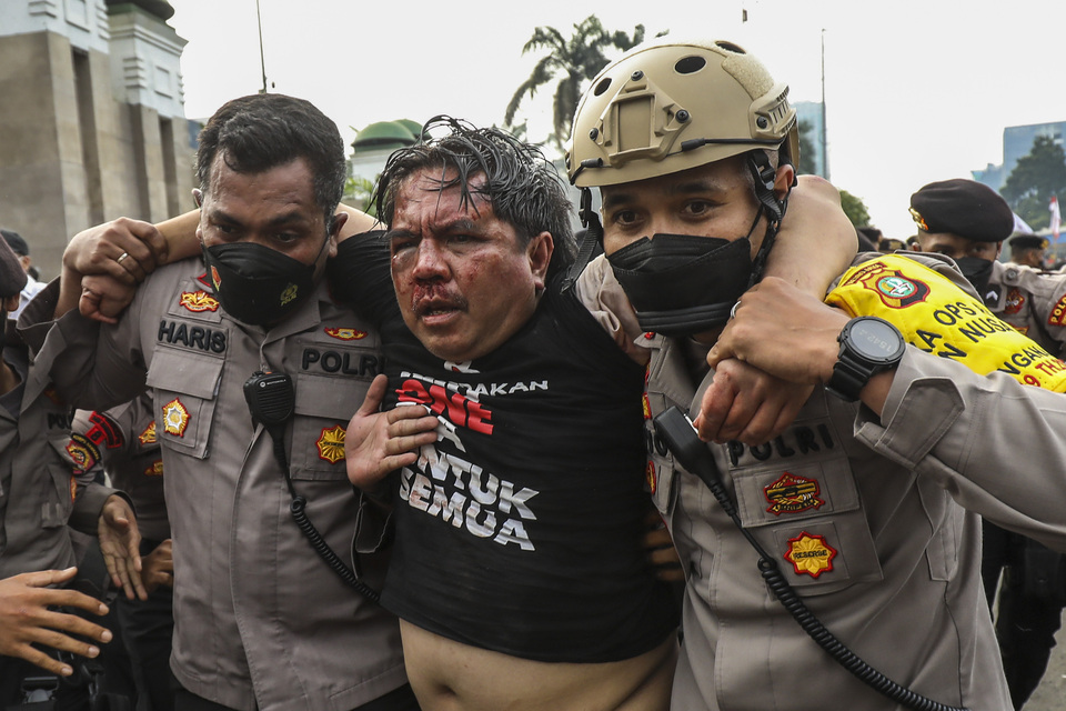 Ade Armando, center, is escorted by police after he was attacked by anti-government protesters in front of the legislature building in Jakarta on April 11, 2022.  (Antara Photo/Galih Pradipta)