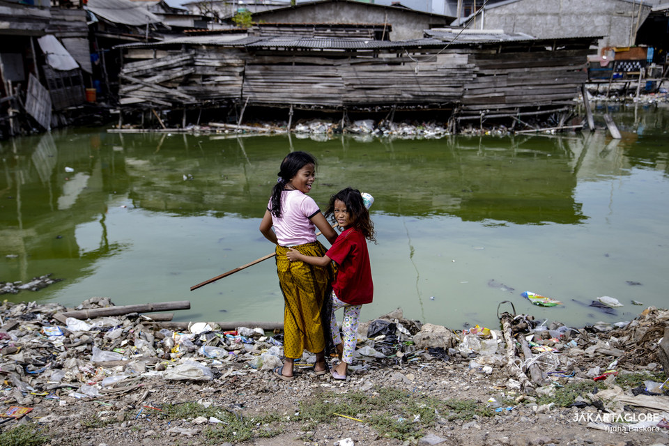 Two girls play by a polluted waterway in Cilincing, North Jakarta on June 23, 2022. (JG Photo/Yudha Baskoro)