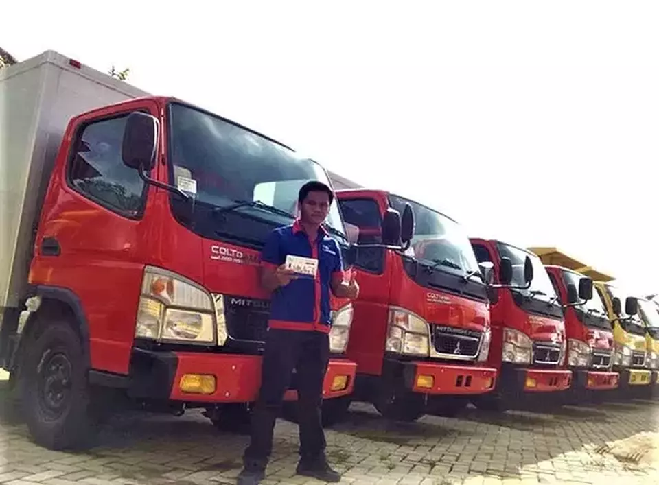 An employee of Sumber Sinergi Makmur poses for a photo in front of a fleet of trucks that have been installed with GPS trackers. (Handout)