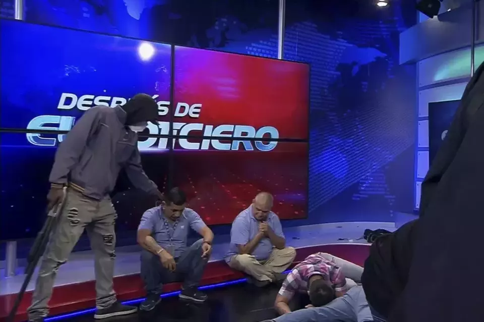 This screen grab of live video from the TC Television network shows a masked, armed person standing over journalists during a live broadcast, in Guayaquil, Ecuador, Tuesday, Jan. 9, 2024. (TC Television network via AP)