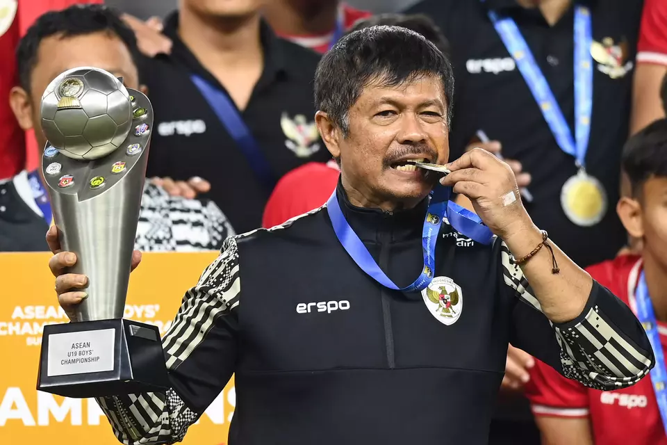 Indonesian coach Indra Sjafri bites his medal and holds the trophy after his team won the ASEAN U19 Boys Championship at Bung Tomo Stadium in Surabaya, East Java, Monday, July 29, 2024, by defeating Thailand 1-0 in the final. (Antara Photo/Sigid Kurniawan)
