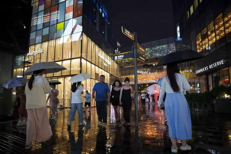 FILE - People walk under the rain with umbrellas at Taikoo Li Sanlitun in Beijing, Tuesday, July 30, 2024. (AP Photo/Vincent Thian, File)