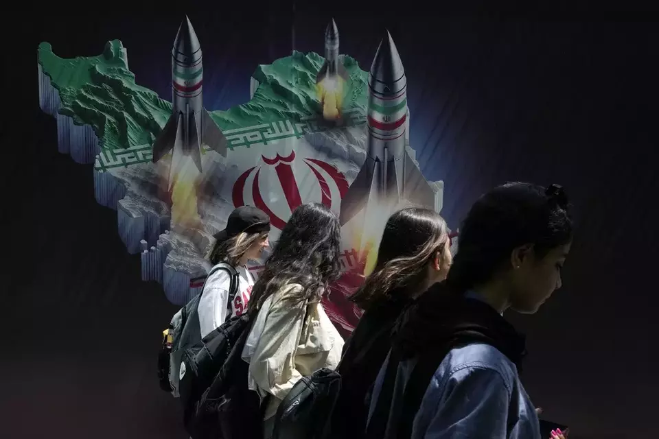 FILE - Iranian women without a mandatory headscarf, or hijab, walk past a banner showing missiles being launched from Iranian map in northern Tehran, Iran, April 19, 2024. (AP Photo/Vahid Salemi, File)