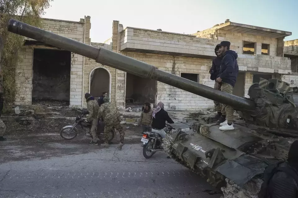 Syrian opposition fighters get on a motorcycle as opposition supporters stand on top of a captured army armored vehicle in the town of Maarat al-Numan, southwest of Aleppo, Syria, Saturday, Nov. 30, 2024. (AP Photo/Omar Albam)