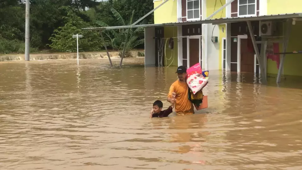 A father and his son navigate floodwaters in The Arthera Hill residential area, Jayasampurna Village, Serangbaru District, Bekasi Regency, West Java, on Tuesday, March 4, 2025. (Beritasatu.com/Ekka Putra)