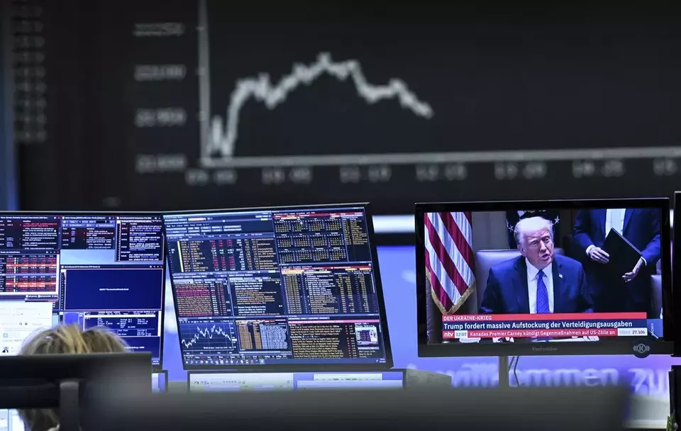 Behind a television monitor showing US President Donald Trump, the display board with the Dax curve shows falling share prices, in Frankfurt, Germany, Thursday, April 3, 2025, after the tariff package announced by US President Trump has pushed share prices sharply into negative territory. (Arne Dedert/dpa via AP)
