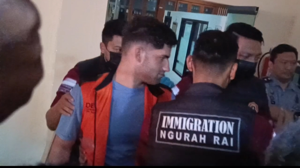US citizen MM is escorted at the Denpasar Class I Immigration Office before a press conference on Monday, April 14, 2025. MM is scheduled for deportation on Monday evening for vandalizing a clinic in Bali. (Beritasatu.com/Sopian Hadi)