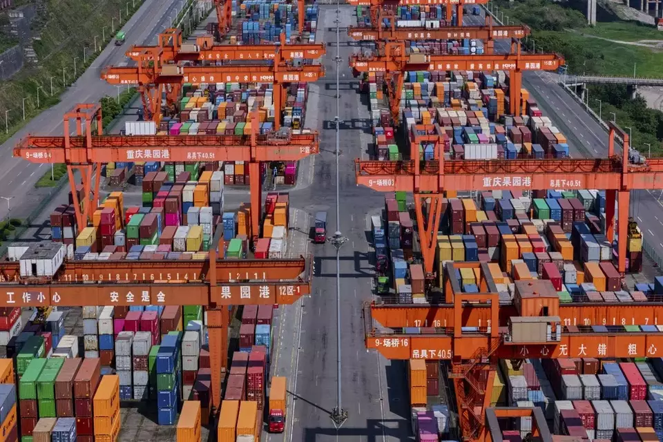 Trucks move past piles of containers stacked at a container terminal port on the Yangtze River in southwest China's Chongqing Municipality on Sunday, April 20, 2025. (Chinatopix Via AP)