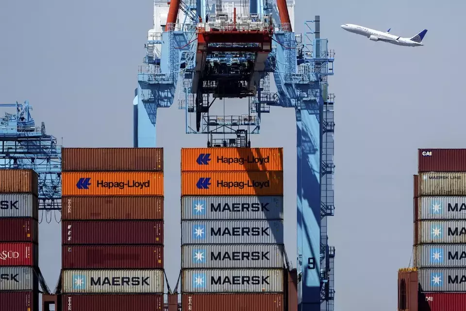 An airplane flies over the container ship Alexandra at the Port Newark Container Terminal, Friday, April 18, 2025, in Newark, N.J. (AP Photo/Julia Demaree Nikhinson)