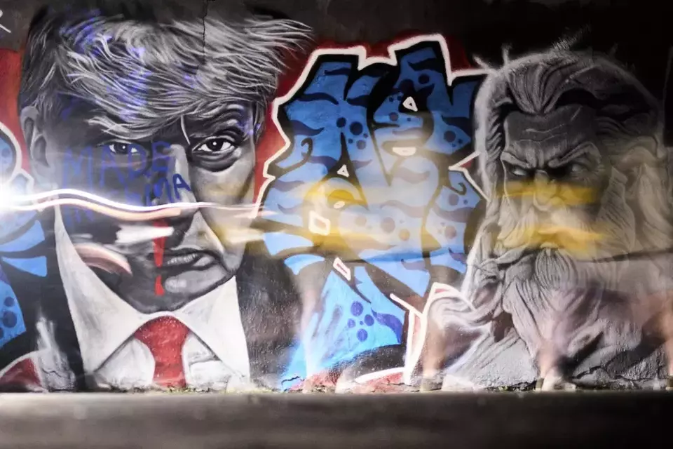 People with flashlights pass a mural of US President Donald Trump, created by graffiti artist EME Freethinker, with the words