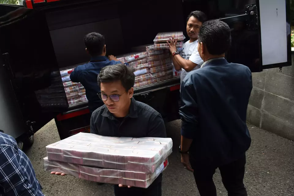 Police officers in plain clothes unload bundles of Rp 100,000 banknotes at the National Police headquarters in Jakarta, Wednesday, May 7, 2025. The banknotes were seized from two suspects in a money laundering case linked to online gambling. (Antara Photo/Indrianto Eko Suwarso)