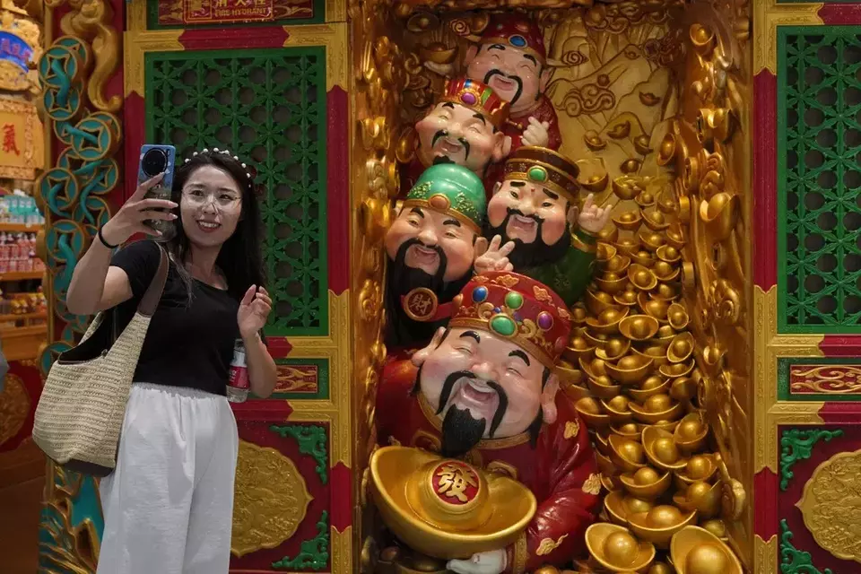 A woman takes a selfie with gods of fortune displayed outside a store selling prosperity items at a shopping mall, in Beijing, Monday, July 14, 2025. (AP Photo/Andy Wong)

