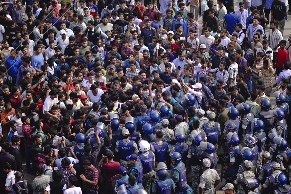 Police officers stand guard as students shout slogans during a protest near the site of the crash of a Bangladesh air force training jet into a school, demanding accountability, compensation for victims' families and the halt of training flights, in Dhaka, Bangladesh, Tuesday, July 22, 2025. (AP Photo/Mahmud Hossain Opu)