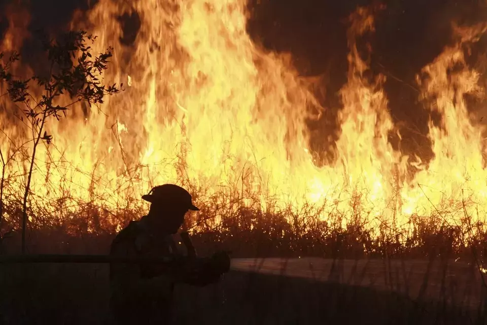 A police officer sprays water in an attempt to extinguish a fire that razes through a peatland field in Ogan Ilir, South Sumatra, Indonesia, Sunday, July 20, 2025. (AP Photo/Muhammad Hatta)

