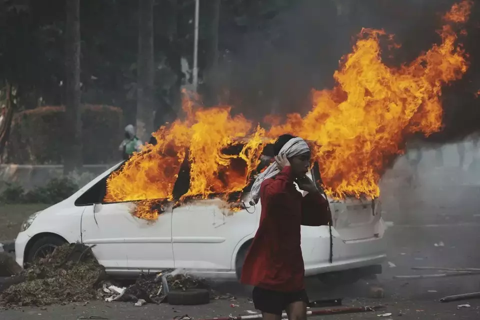 A man walks past a burning car during a protest following the death of a delivery rider in clashes between riot police and students protesting against lawmakers' allowances, in Jakarta, Indonesia, Friday, Aug. 29, 2025. (AP Photo/Achmad Ibrahim)