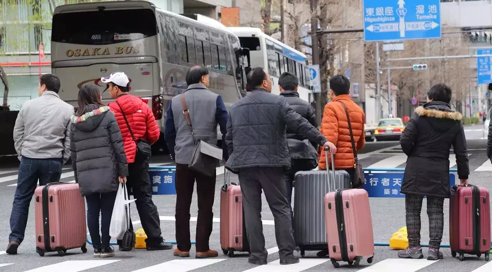 FILE - Chinese tourists wait for a bus at Tokyo's Ginza shopping district in Tokyo, Saturday, March 12, 2016. (AP Photo/Koji Sasahara, File)