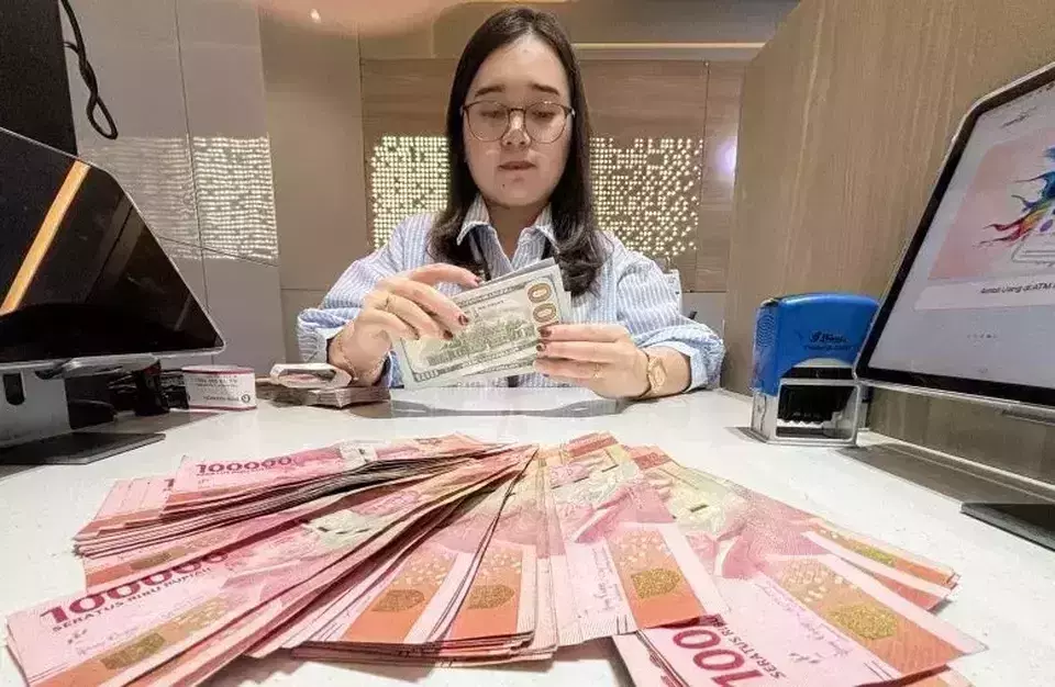 Bank teller counts US dollar banknotes at a currency exchange counter, with stacks of Indonesian rupiah laid out on the desk in Jakarta. Dec. 22, 2025. (Antara Photo/Rivan Awal Lingga/rwa)