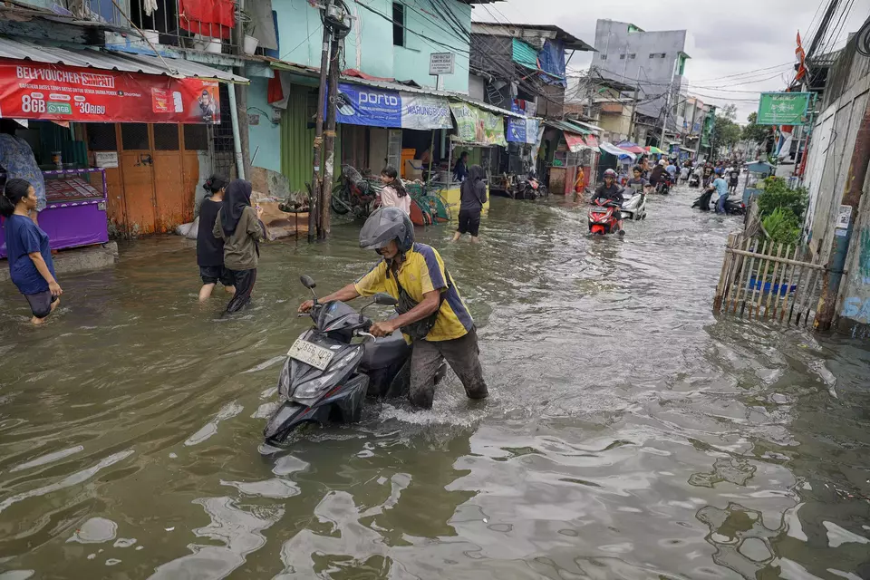 A man pushes his scooter along a flooded road in Kapuk Muara, North Jakarta, on Sunday, Jan. 18, 2026. (B-Universe Photo/Joanito De Saojoao)