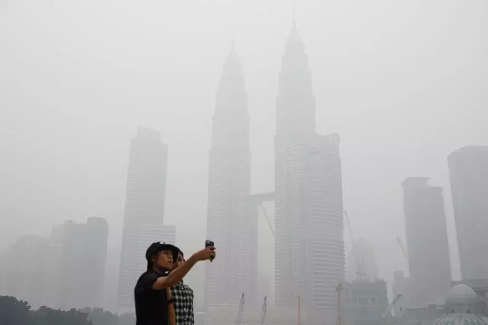FILE -Tourists take a selfie against Malaysia's landmark building Petronas Twin Towers shrouded with haze in Kuala Lumpur, Malaysia on Sept. 26, 2015. (AP Photo/Joshua Paul, File)
