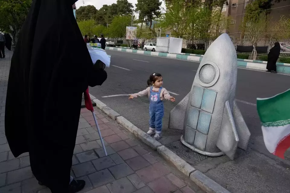 A girl stands next to a replica of a spacecraft in a memorial for school children who were killed during a strike on a school in the southern town of Minab on Feb. 28, in downtown Tehran, Iran, Tuesday, April 7, 2026. (AP Photo/Vahid Salemi)